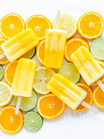 Overhead shot of five orange coloured popsicles displayed on top of orange, lemon and lime slices.