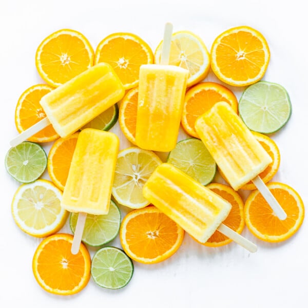 Overhead shot of five orange coloured popsicles displayed on top of orange, lemon and lime slices.