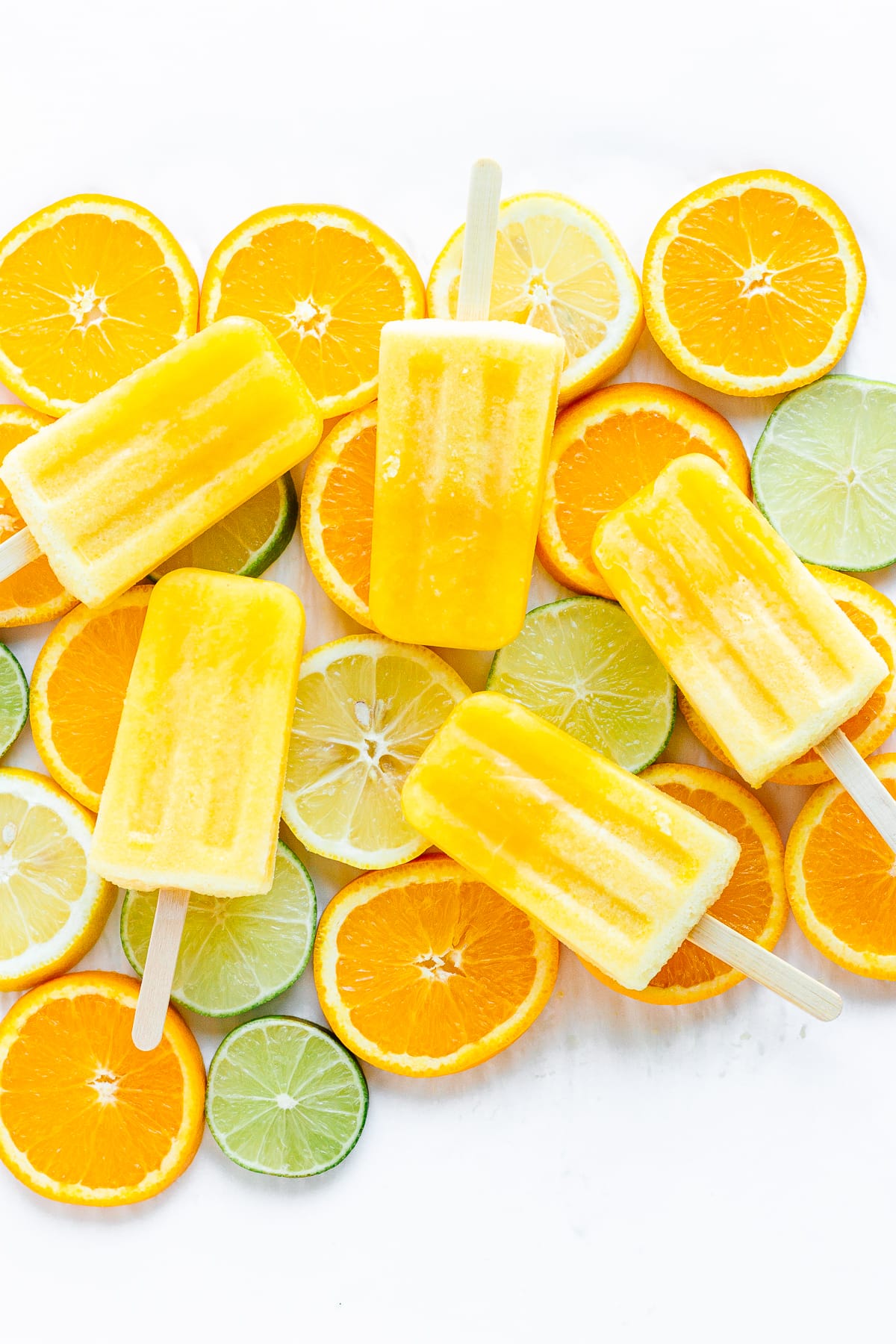 Five orange lemon lime popsicles displayed on top of a variety of sliced citrus.