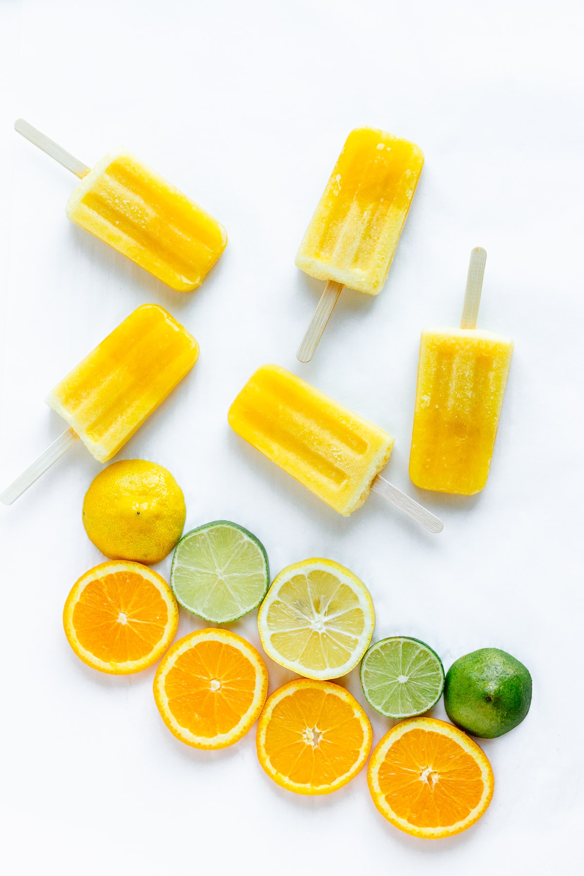 Overhead shot of five orange lemon lime popsicles next to a variety of sliced citrus.