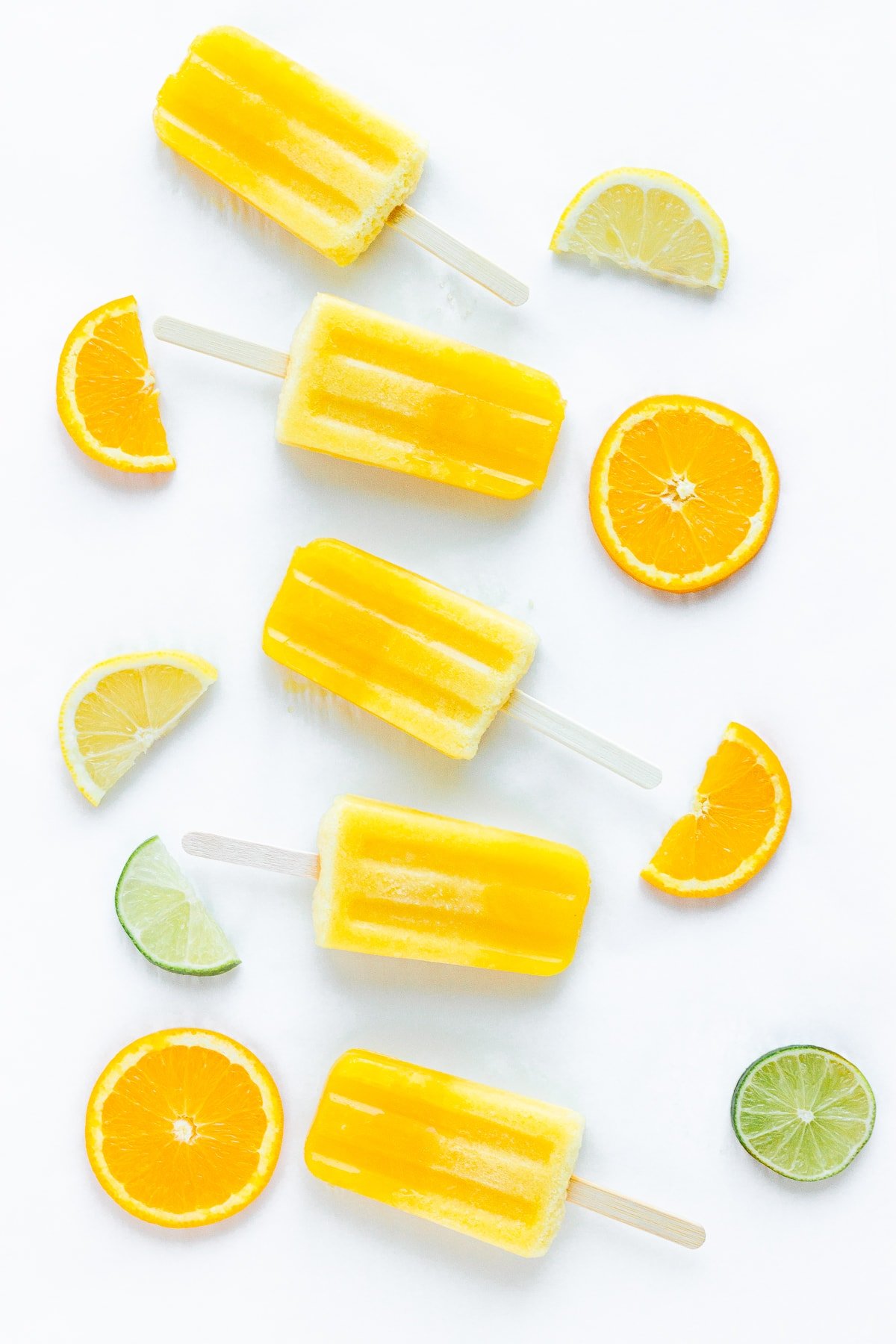 Overhead photo of orange lemon lime popsicles with a variety of citrus slices next to them.