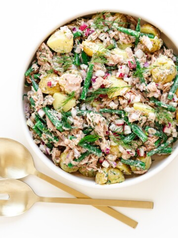 Overhead photo of a bowl of tuna potato salad with gold coloured salad servers next to it.