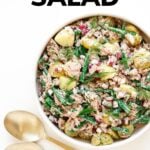 Bowl of salad with gold salad servers and text overlay that reads "Tuna Potato Salad".