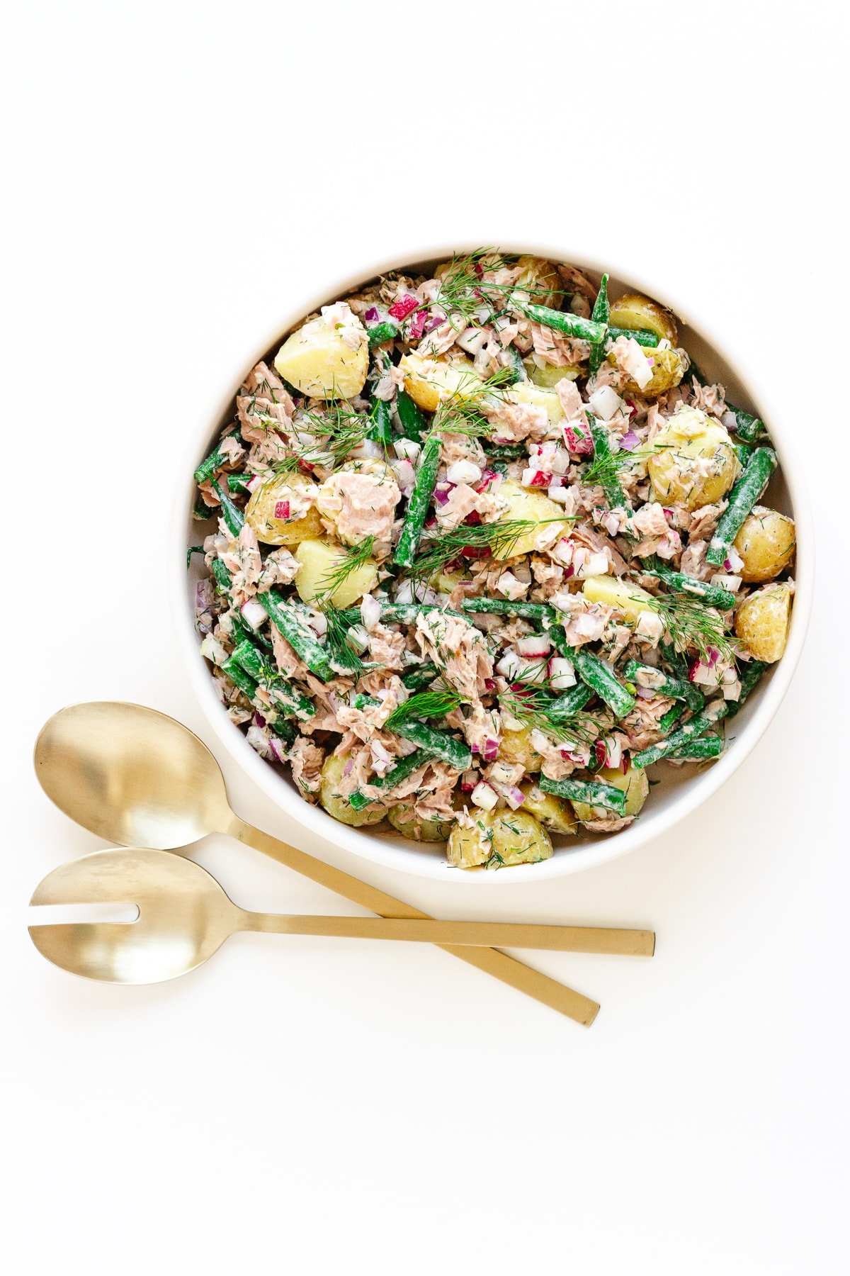 White bowl of tuna potato salad with gold salad servers next to it.