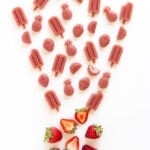 Variety of strawberry gummies in different shapes and a couple fresh strawberries on a white background.