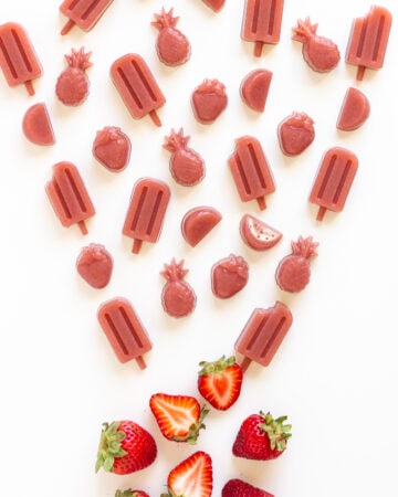 Variety of strawberry gummies in different shapes and a couple fresh strawberries on a white background.