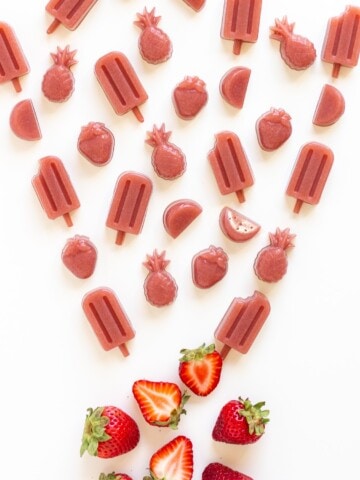 Variety of strawberry gummies in different shapes and a couple fresh strawberries on a white background.