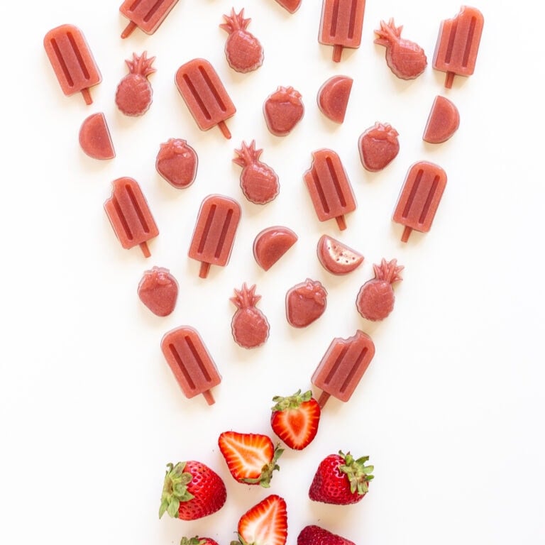 Variety of strawberry gummies in different shapes and a couple fresh strawberries on a white background.