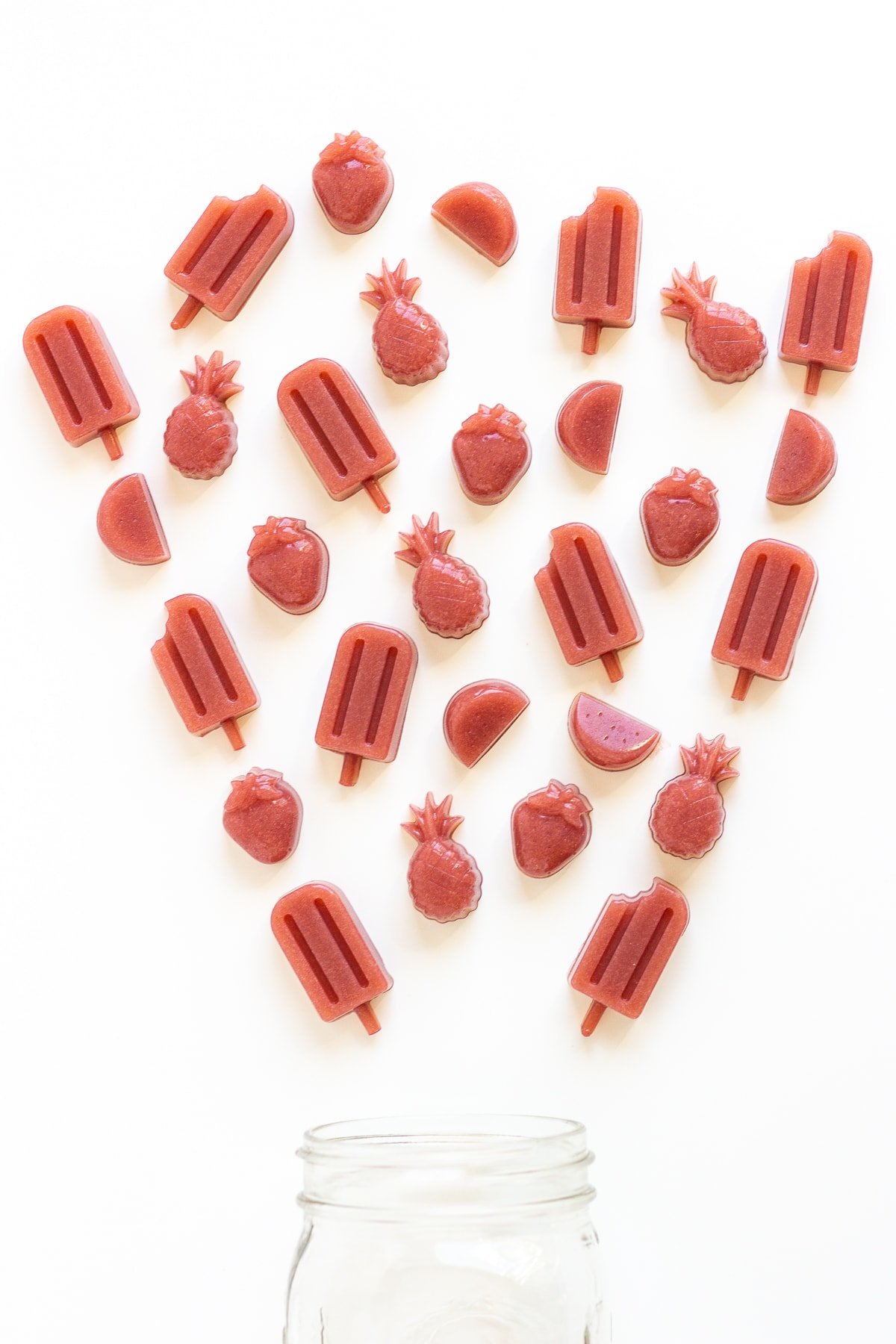 Overhead shot of jar with a variety of different shaped homemade gummies spilling out.