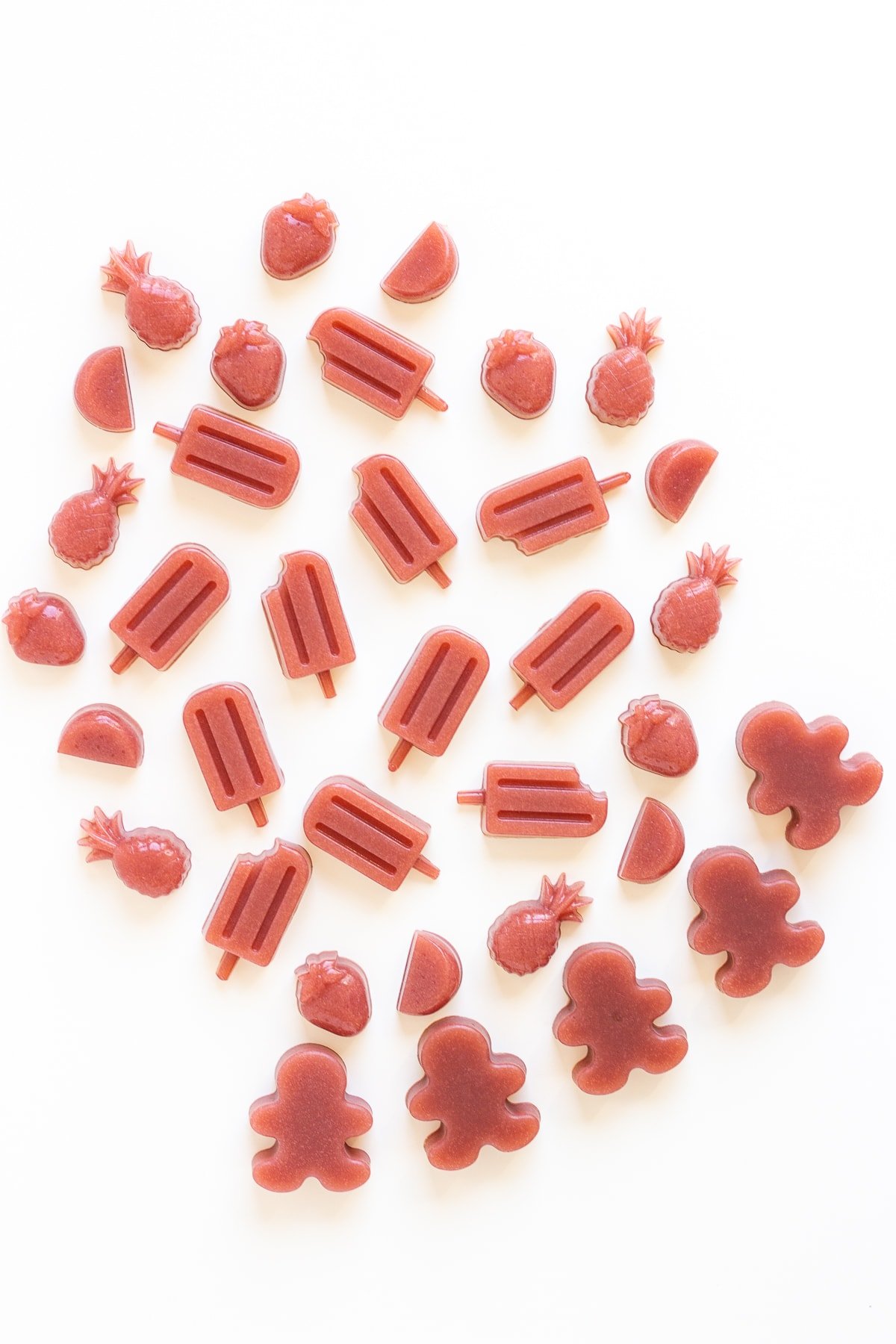 Different shapes of homemade strawberry gummies scattered on a white background