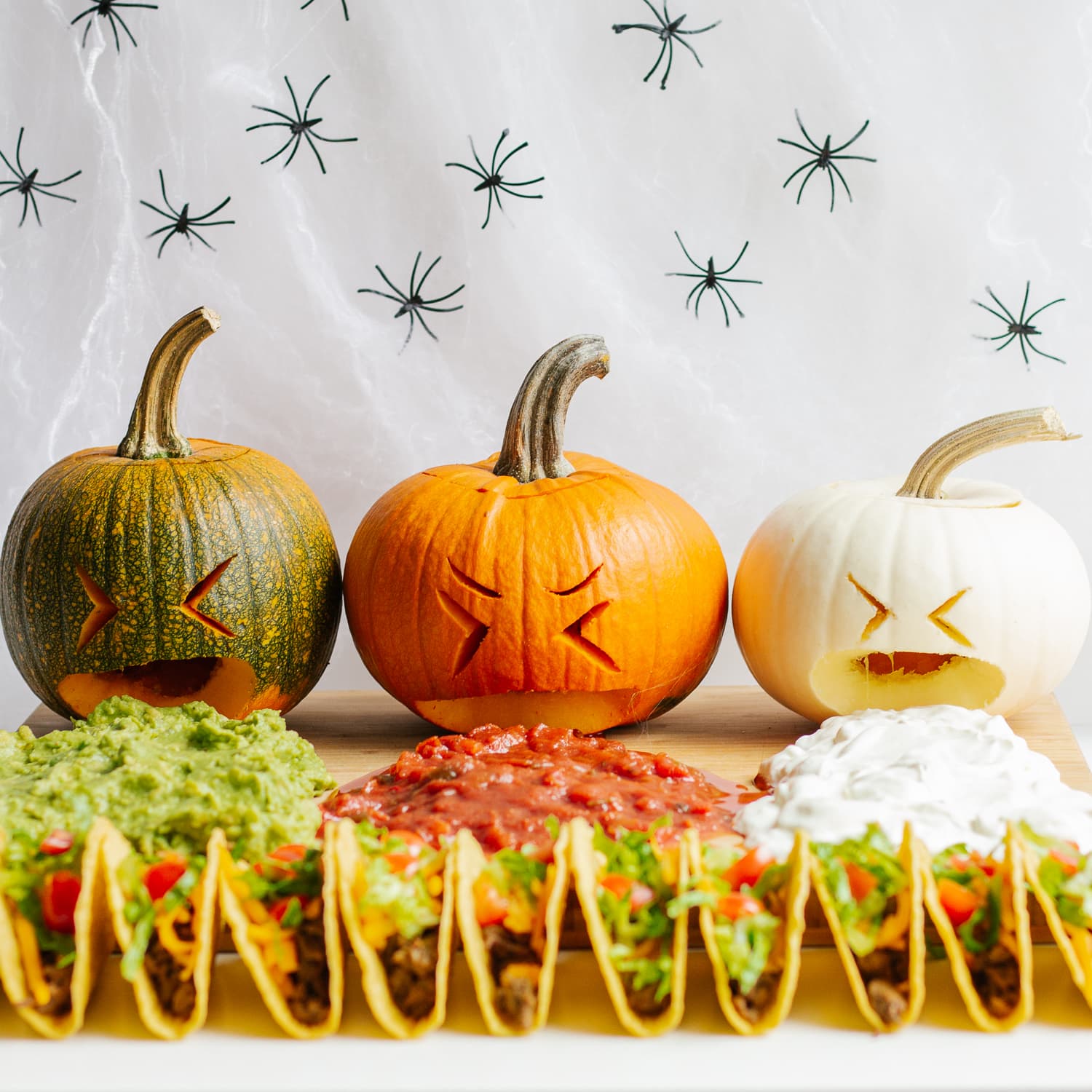 Halloween themed taco board with three pumpkins puking guacamole, salsa and sour cream.