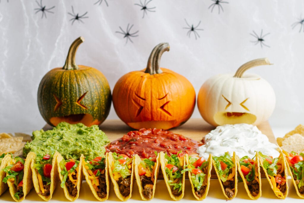 A Halloween taco board featuring three topping puking pumpkins.