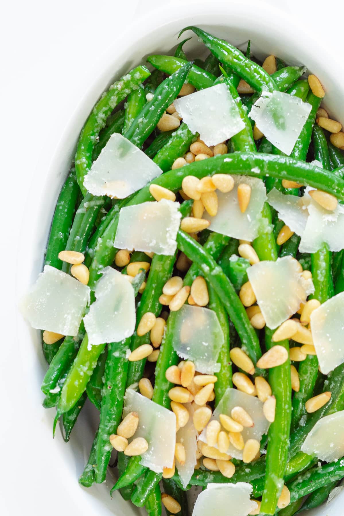 Close up photo of garlic butter green beans with parmesan and pine nuts scattered on top.