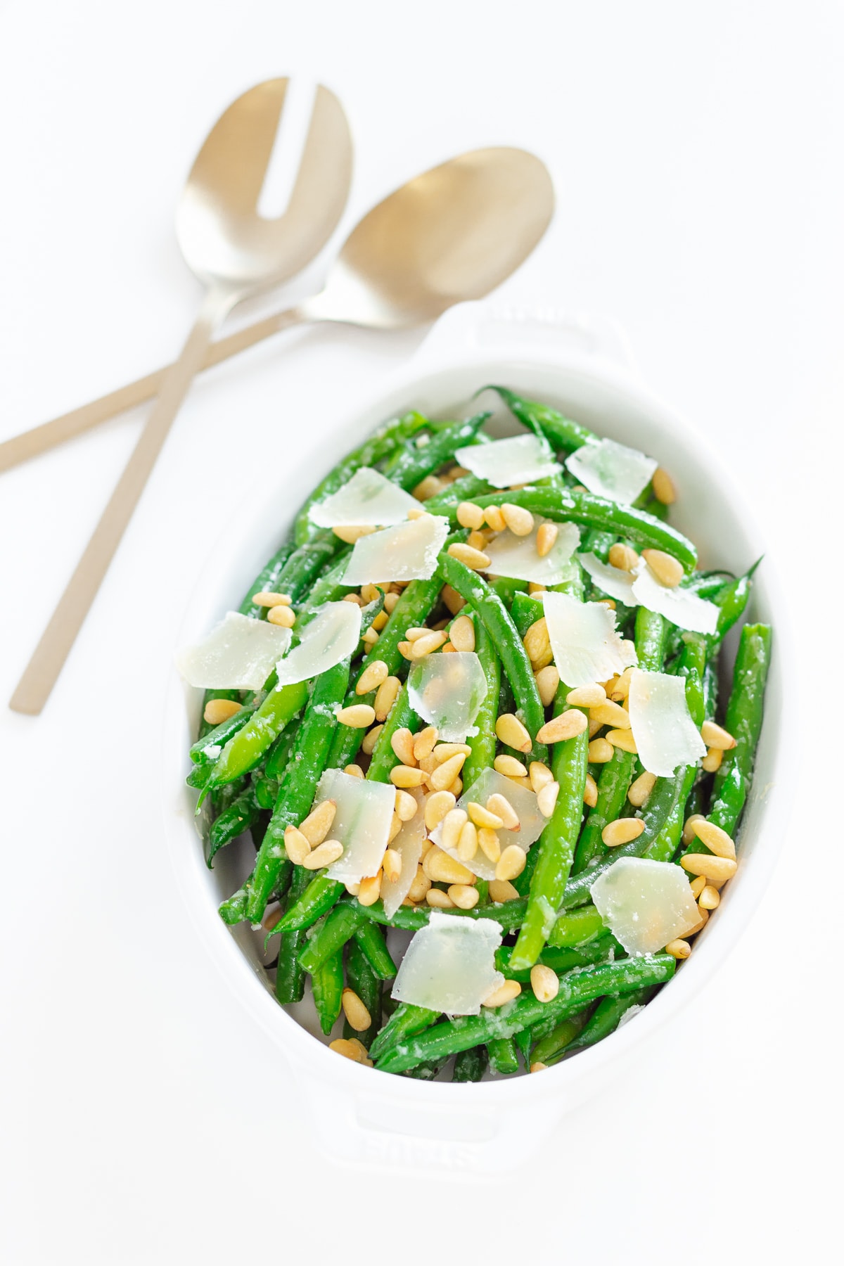 Dish of garlic butter green beans with gold serving spoons next to it.