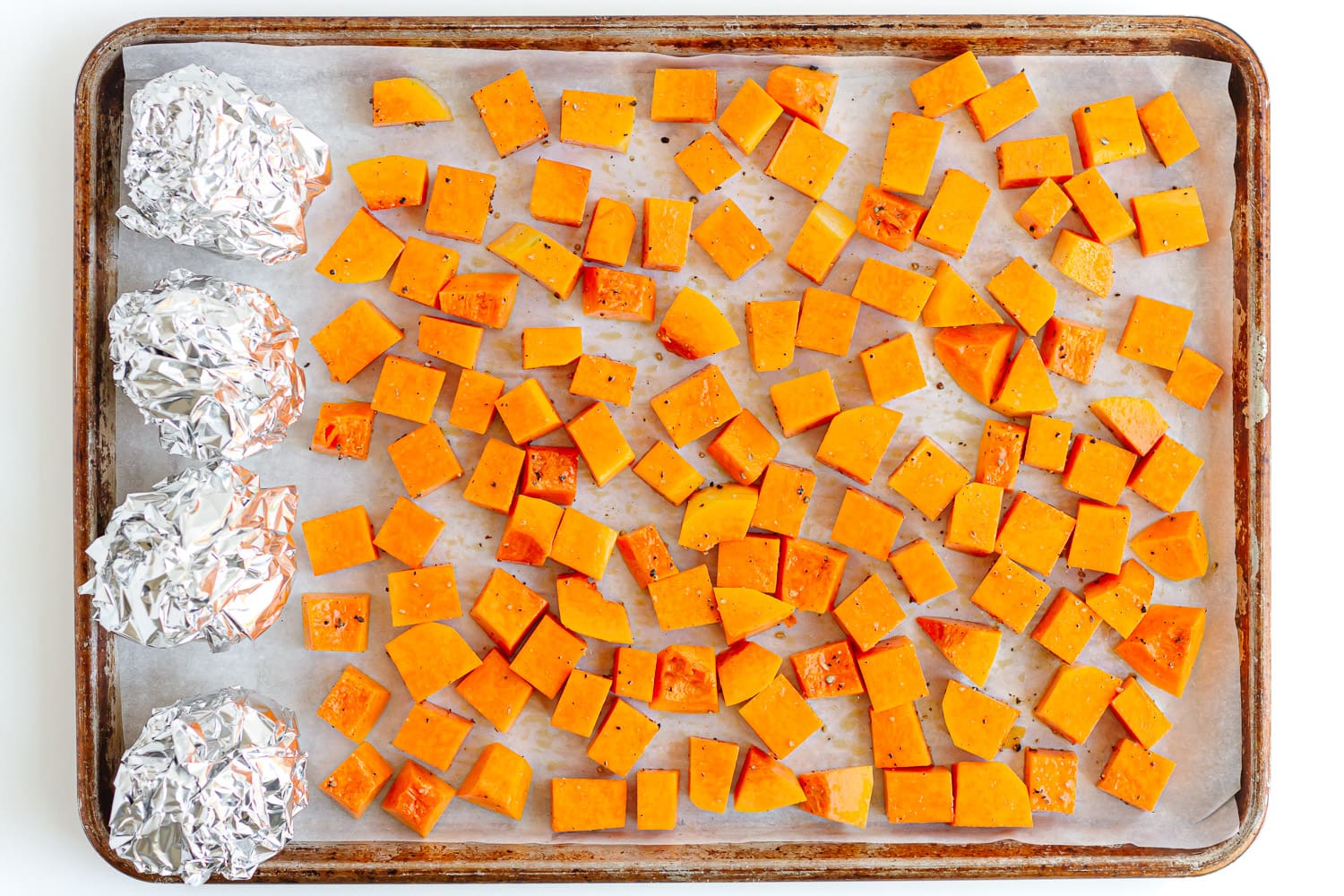 Cubed pumpkin and beets wrapped in foil on a lined baking sheet.