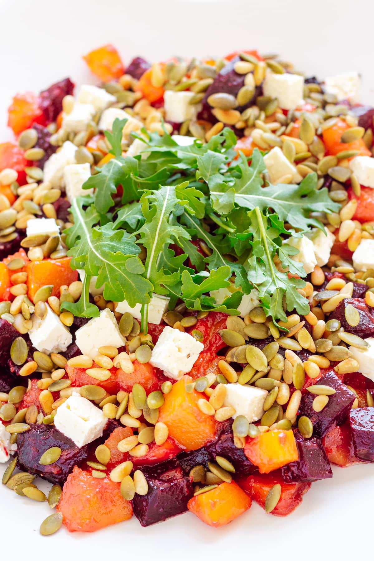 Close up photo of roasted pumpkin and beetroot salad topped with feta cheese, pine nuts, pepitas and arugula.