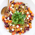 Overhead photo of roasted pumpkin and beetroot salad topped with feta, pine nuts, pepitas and arugula.