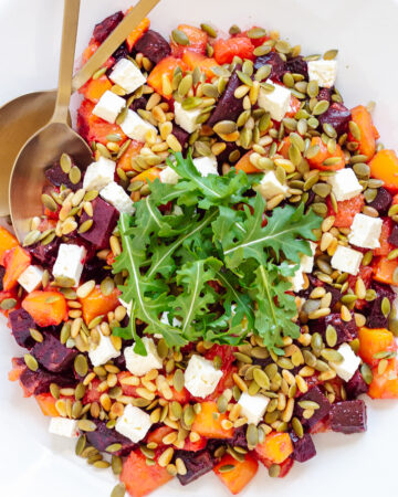 Overhead photo of roasted pumpkin and beetroot salad topped with feta, pine nuts, pepitas and arugula.