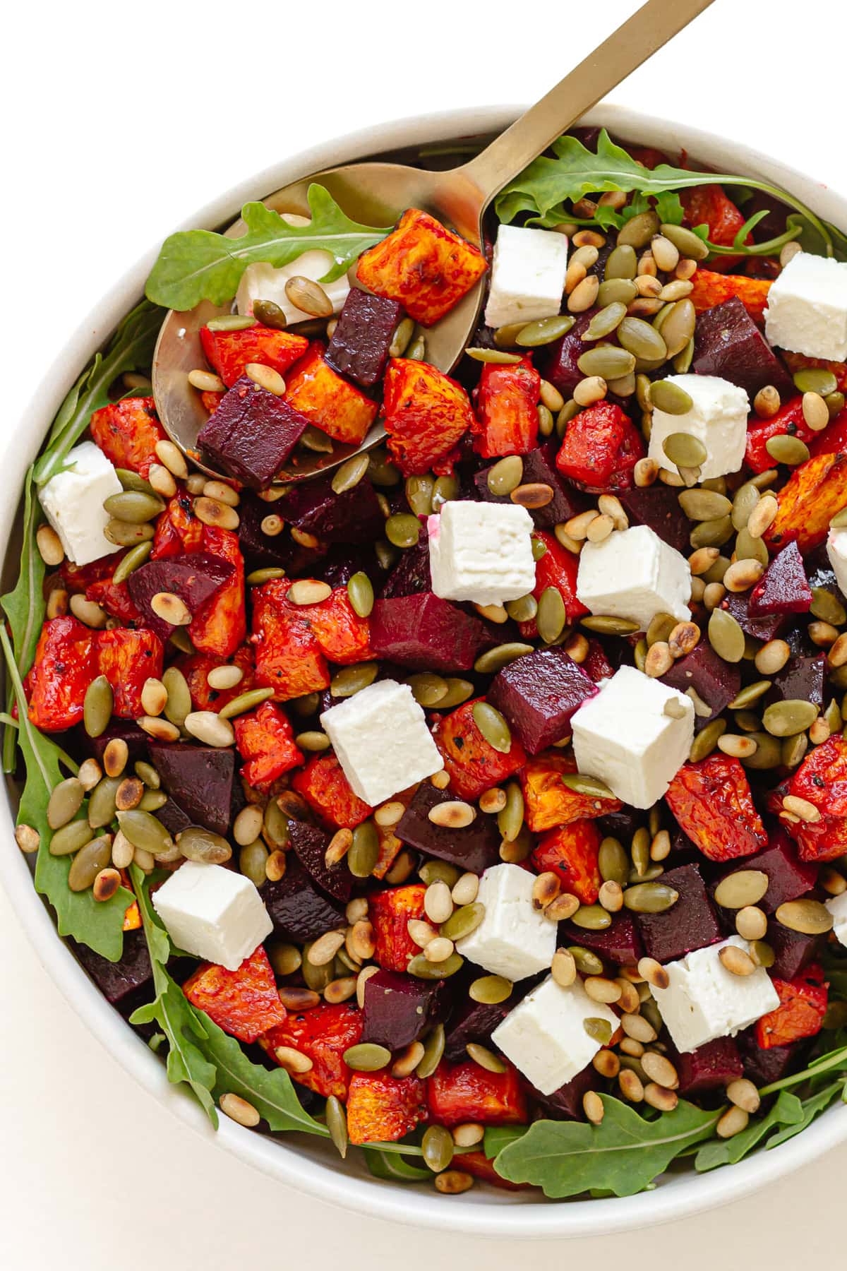 Roasted pumpkin and beetroot salad in a serving bowl with gold colored serving spoon.