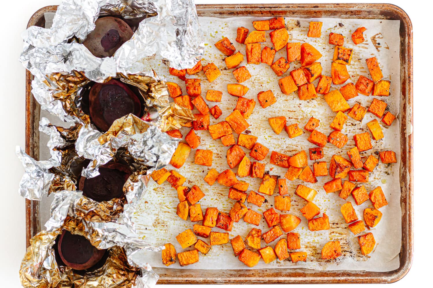 Roasted cubed pumpkin and whole beets on a baking sheet.