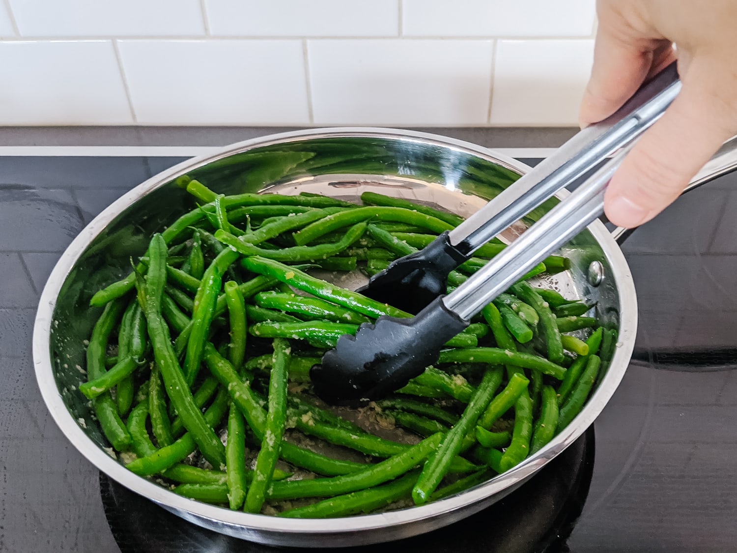 Green beans in a large pan being tossed with tongs.