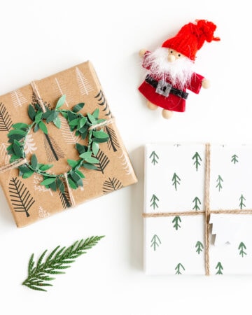 Flat lay image of two Christmas gifts, Santa ornament and a small evergreen branch on a white background.