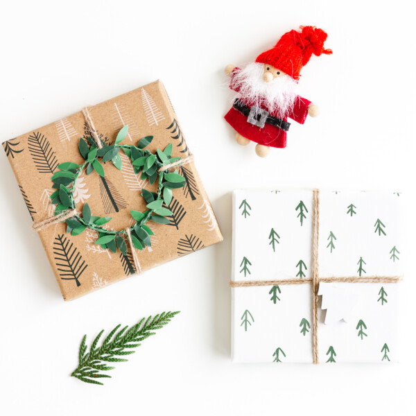 Flat lay image of two Christmas gifts, Santa ornament and a small evergreen branch on a white background.