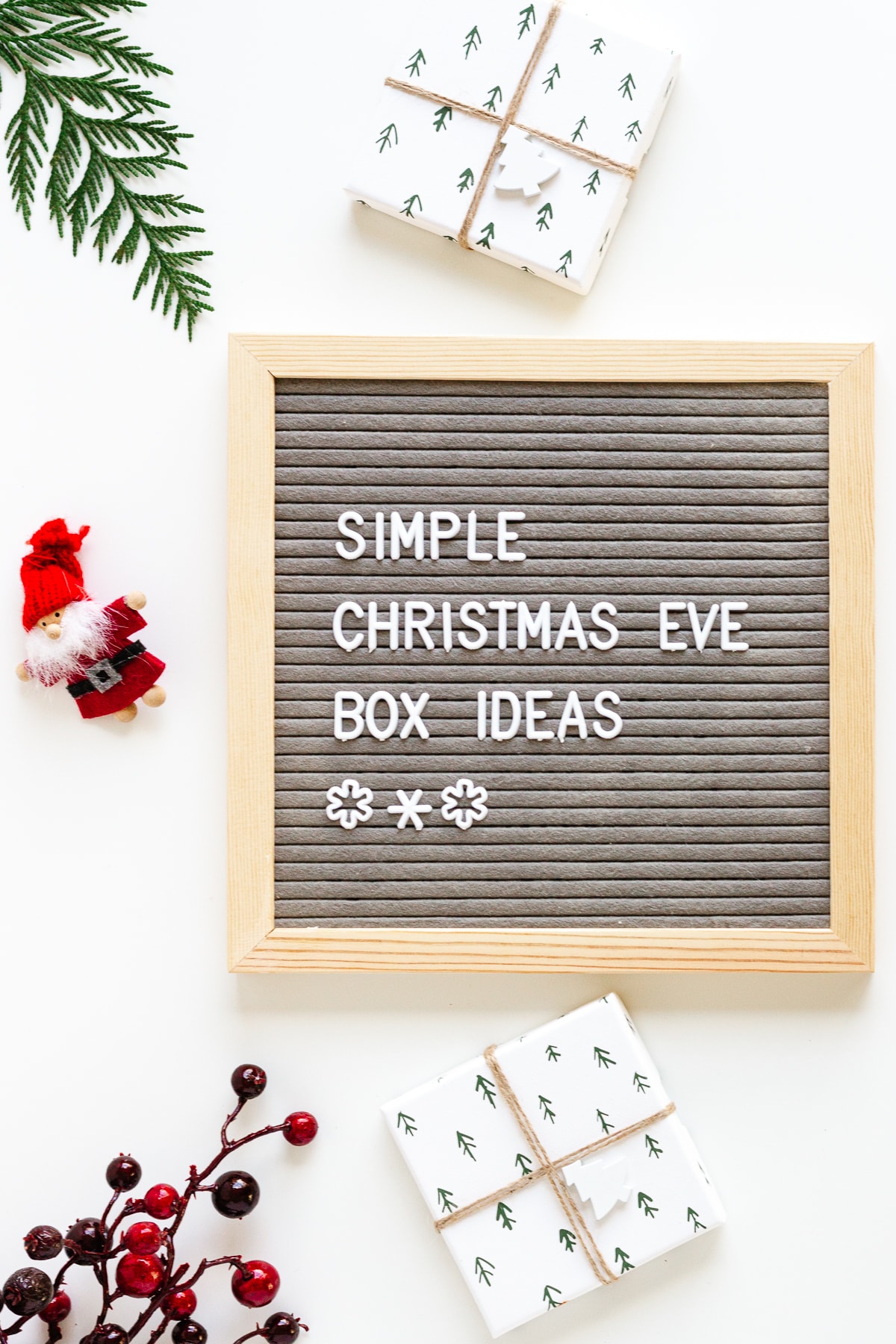 Flatlay photo of a letterboard that says "Simple Christmas Eve Box Ideas" surrounded by some gifts and christmas decor items.