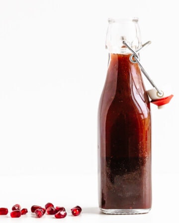Glass bottle of pomegranate salad dressing with a few pomegranate arils scattered next to it.