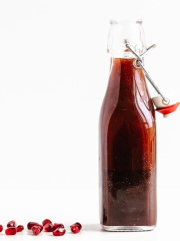 Glass bottle of pomegranate salad dressing with a few pomegranate arils scattered next to it.