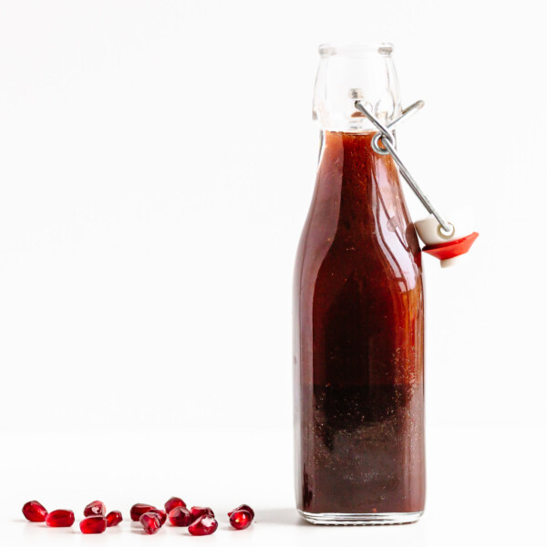 Glass bottle of pomegranate salad dressing with a few pomegranate arils scattered next to it.