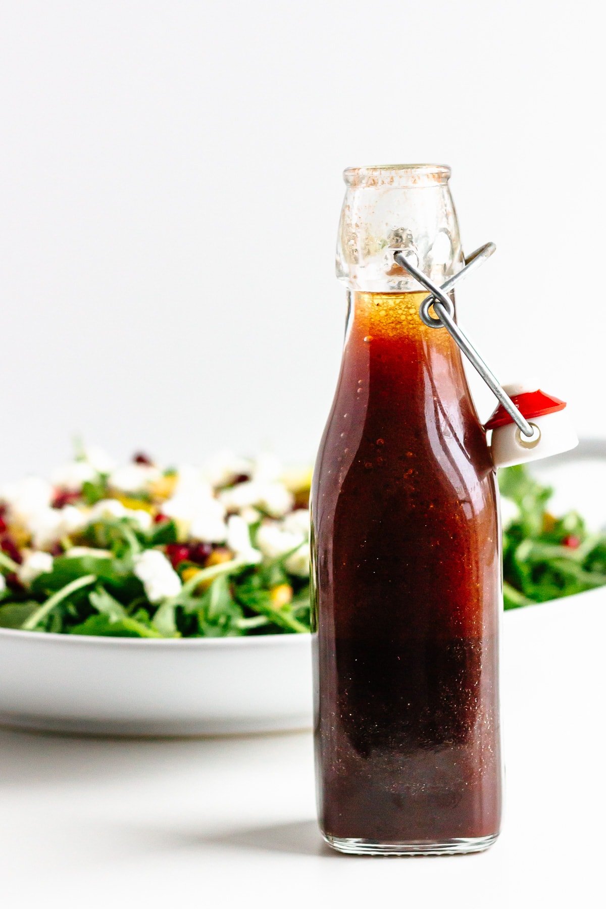 Glass bottle of pomegranate salad dressing with plate of salad in the background.