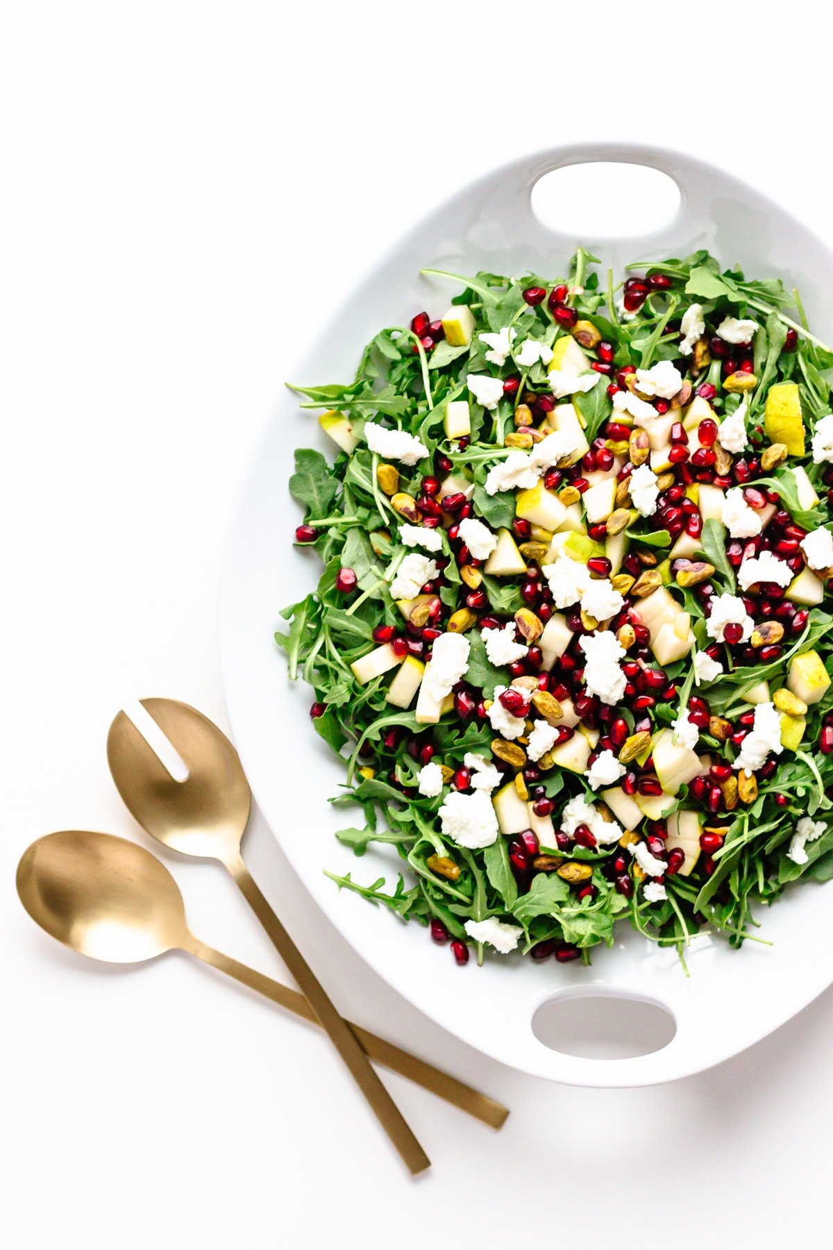 Winter salad on a large white platter with matte gold coloured salad servers next to it.