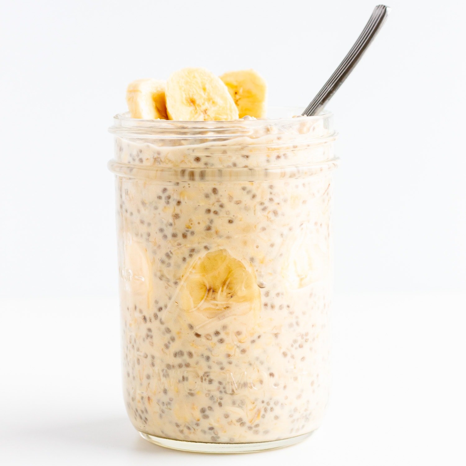 A mason jar of banana overnight oats garnished with fresh banana slices and a spoon sticking out.