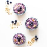 Three containers of blueberry overnight oats with blueberries and rolled oats scattered beside them.