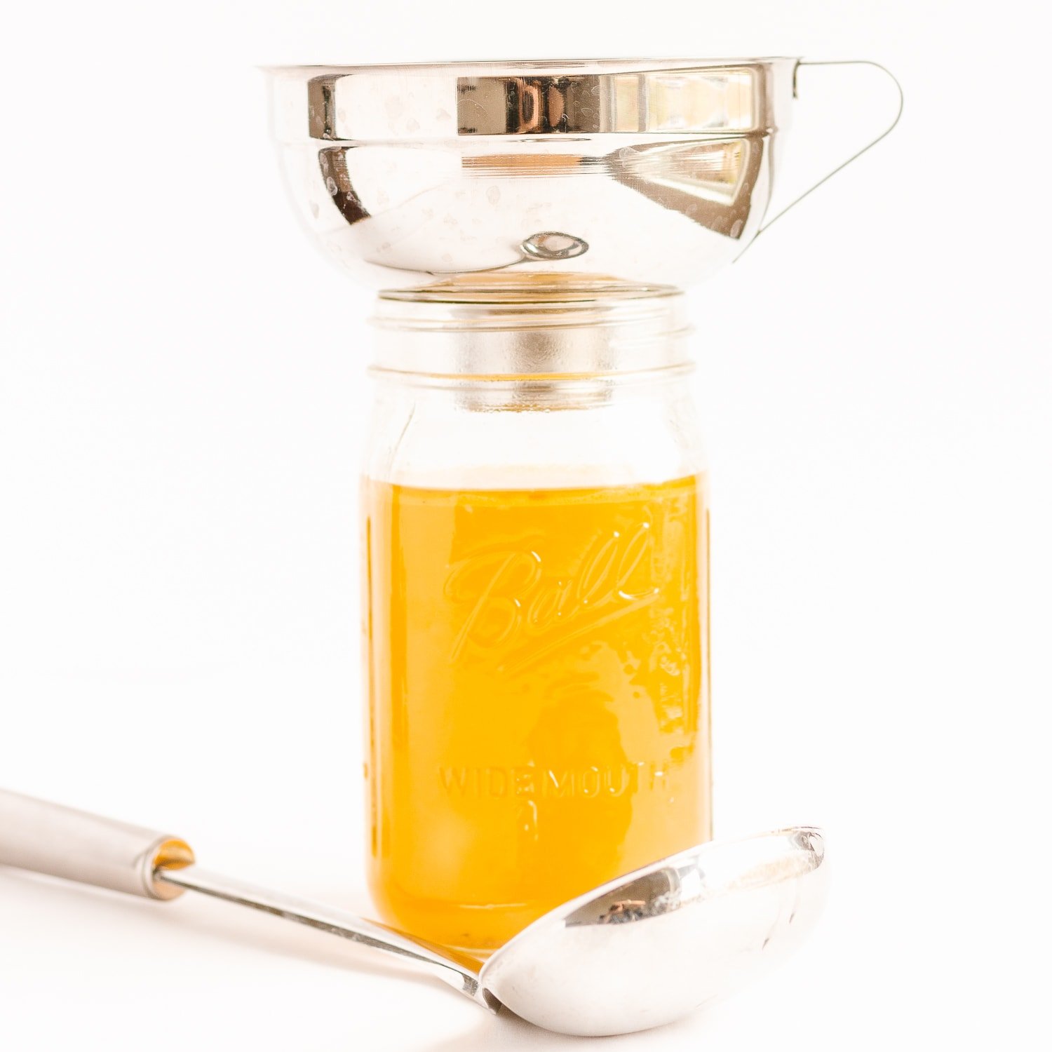 Mason jar being filled with broth using a wide mouth funnel.