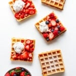 Overhead of multiple square waffles on a white background with different toppings.