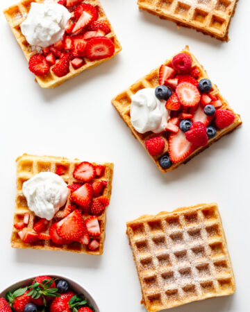 Overhead of multiple square waffles on a white background with different toppings.