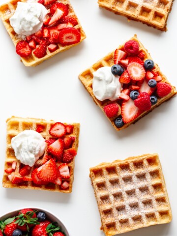 Overhead of multiple square waffles on a white background with different toppings.