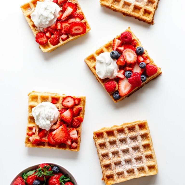 Overhead of multiple square waffles on a white background with different toppings.