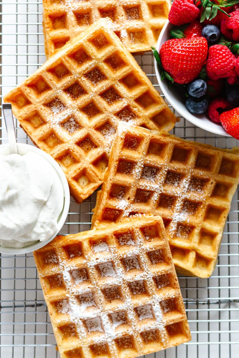 German waffles on a wire cooling rack with a bowl of whipped cream and mixed berries.