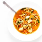 Vegetable soup in a white bowl with spoon.