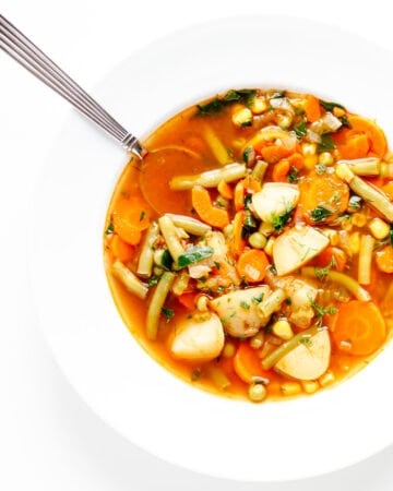 Vegetable soup in a white bowl with spoon.