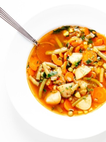 Vegetable soup in a white bowl with spoon.