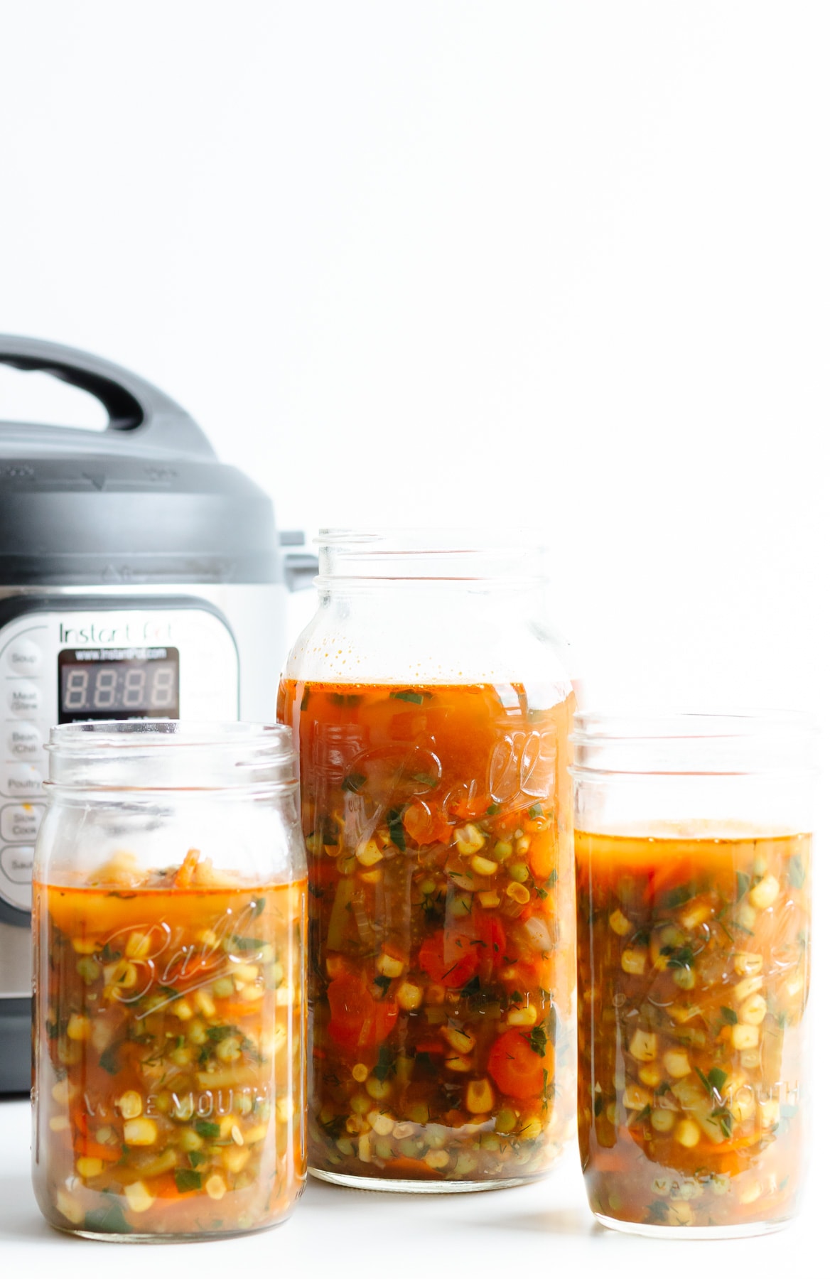 Three jars of vegetable soup standing in front of an Instant Pot.