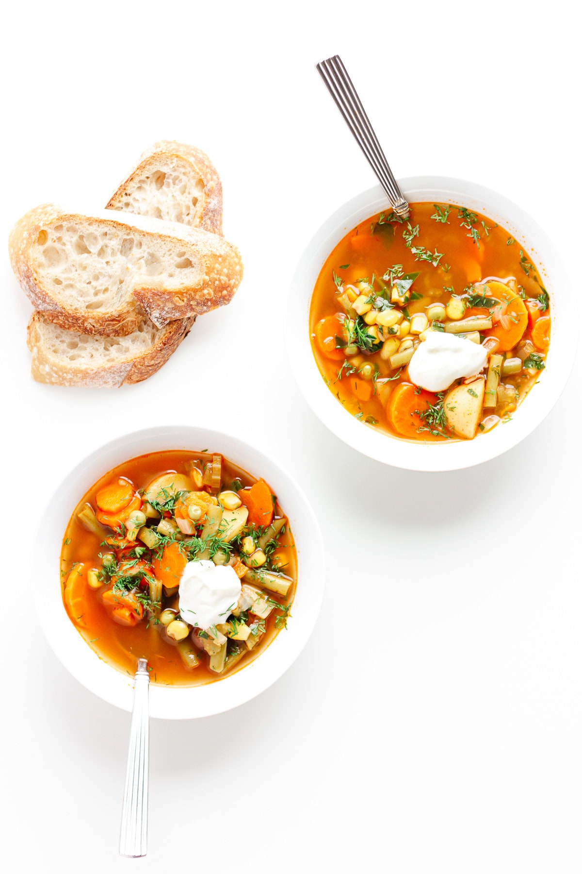 Two bowls of vegetable soup next to two slices of bread.