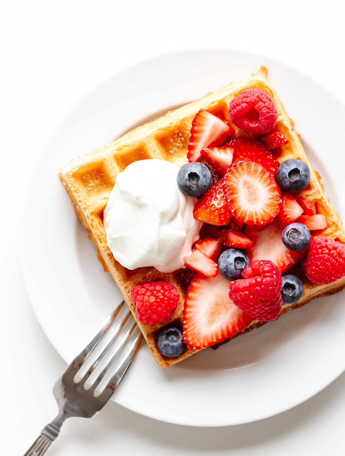 Square waffle topped with mixed berries and a dollop of whipped cream on a white plate.