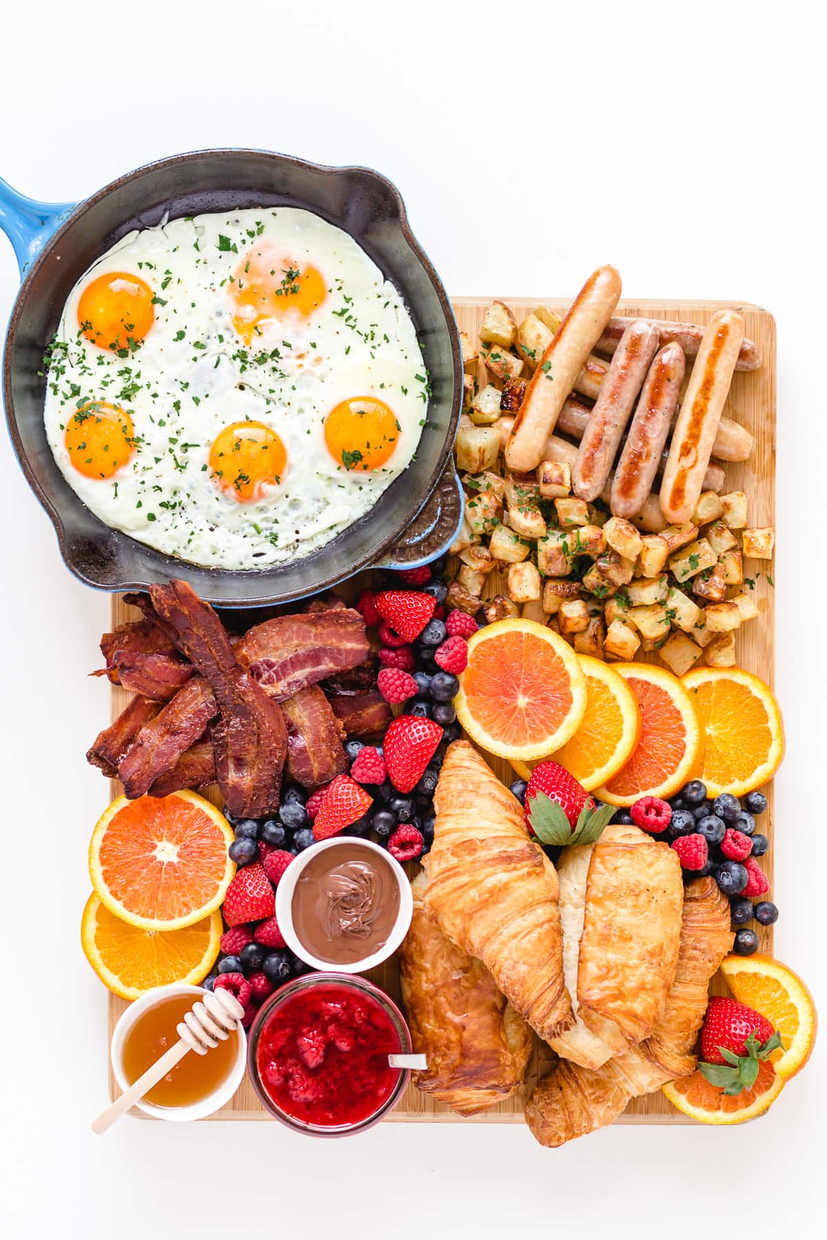 Bacon and eggs breakfast grazing board featuring fried eggs, bacon, breakfast sausages, croissants, hash browns, fresh fruit and spreads.