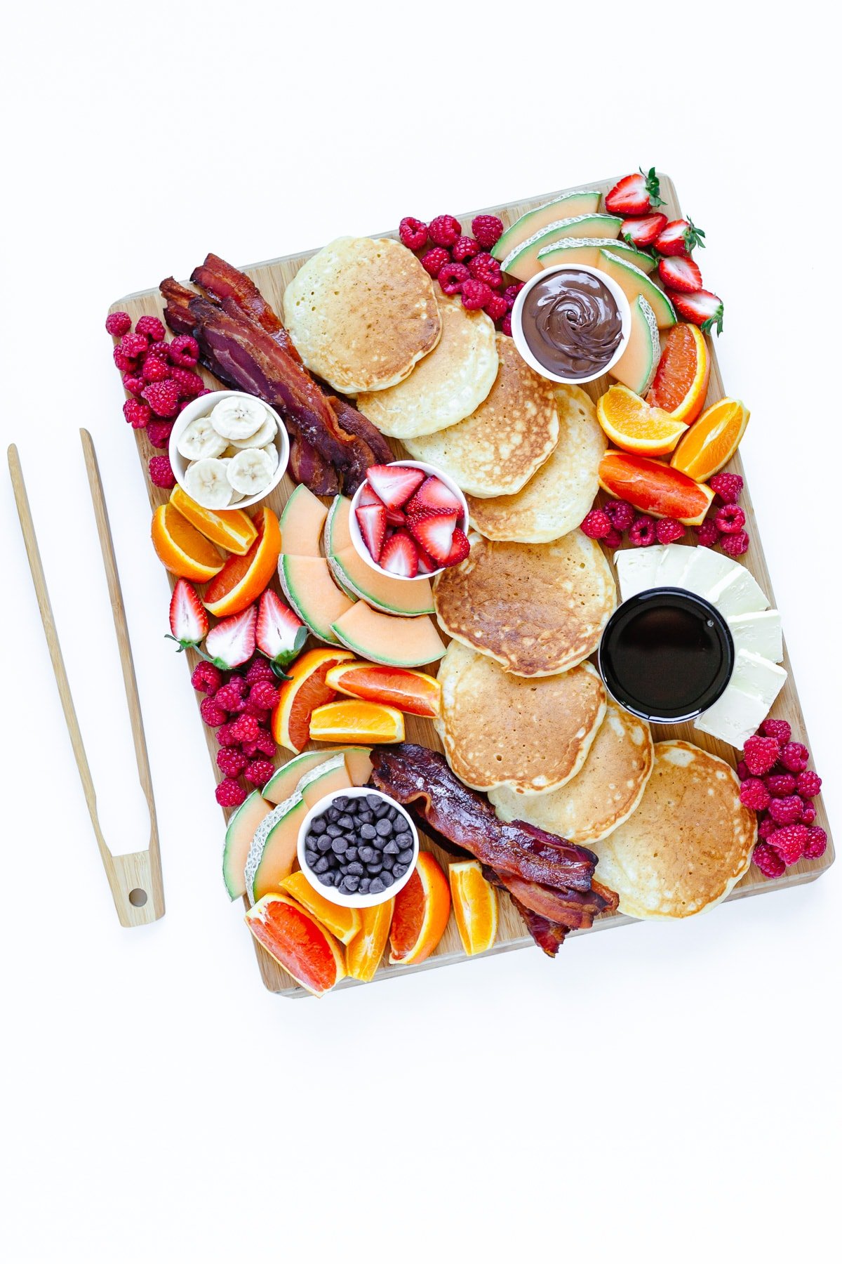 Pancake charcuterie board and wooden tongs on a white background.