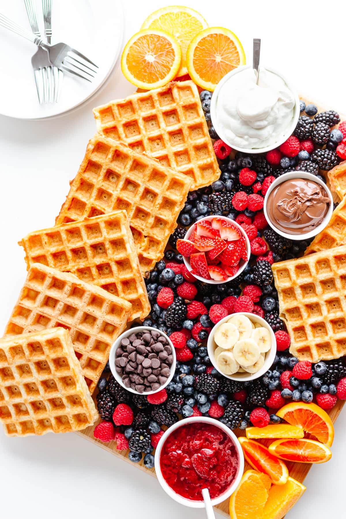 Waffle breakfast board with pile of plates and forks in the corner.